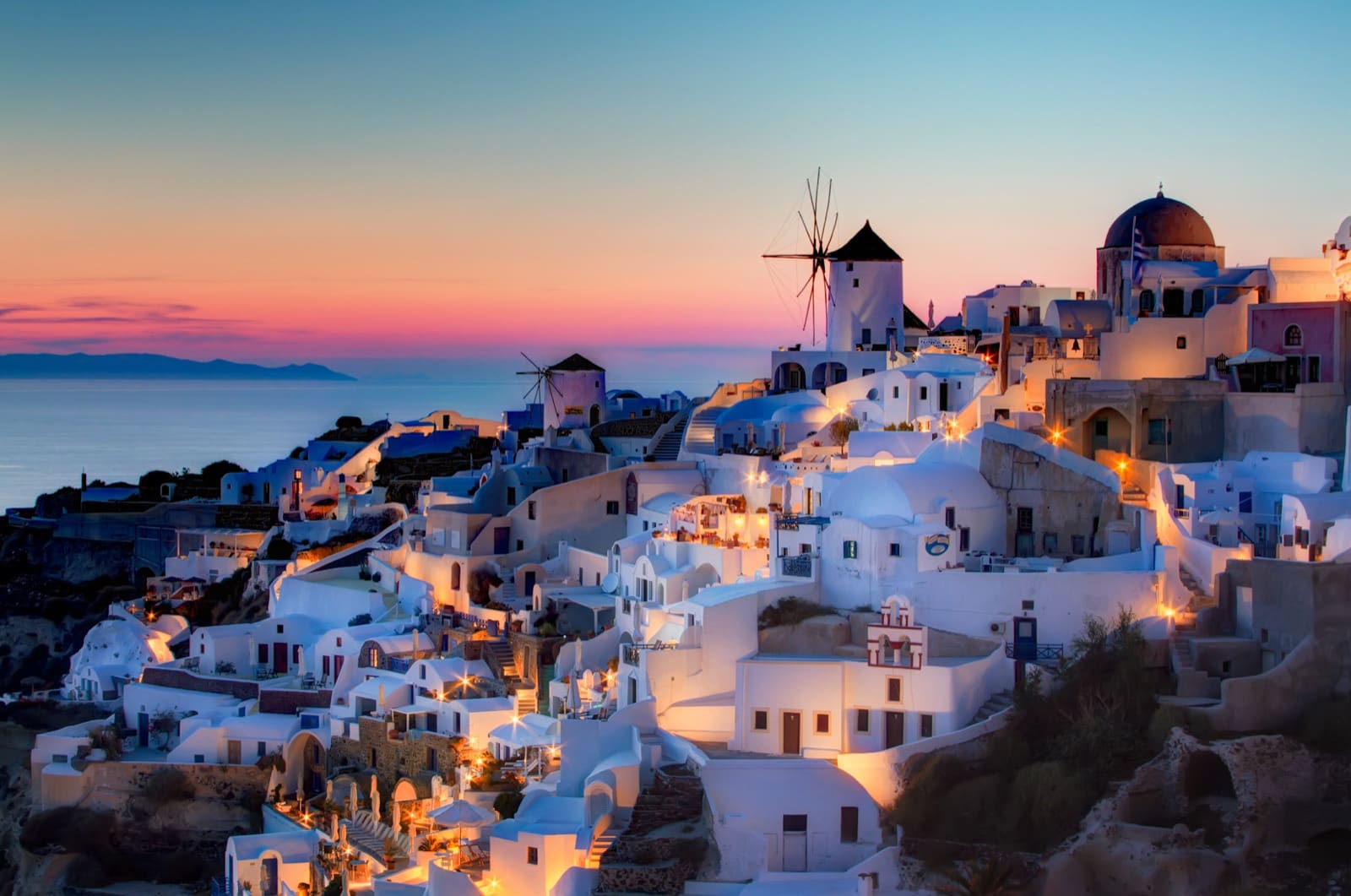 Whitewashed houses and blue domes of Oia tumbling down the Santorini caldera at sunset